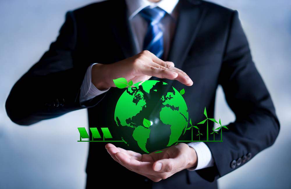 Businessman in suit and tie holding a virtual green earth with solar panels and windmills to represent corporate sustainability