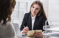 A smiling HR manager takes notes while interviewing a prospective candidate.